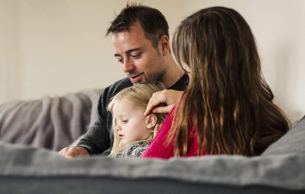 Two parents and a toddler sitting on a sofa together.